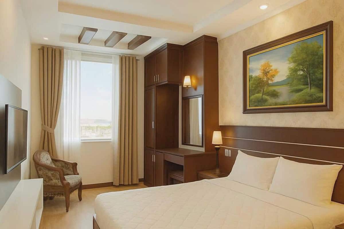 A hotel room with a large bed, a desk with a chair, a television, and a painting on the wall.