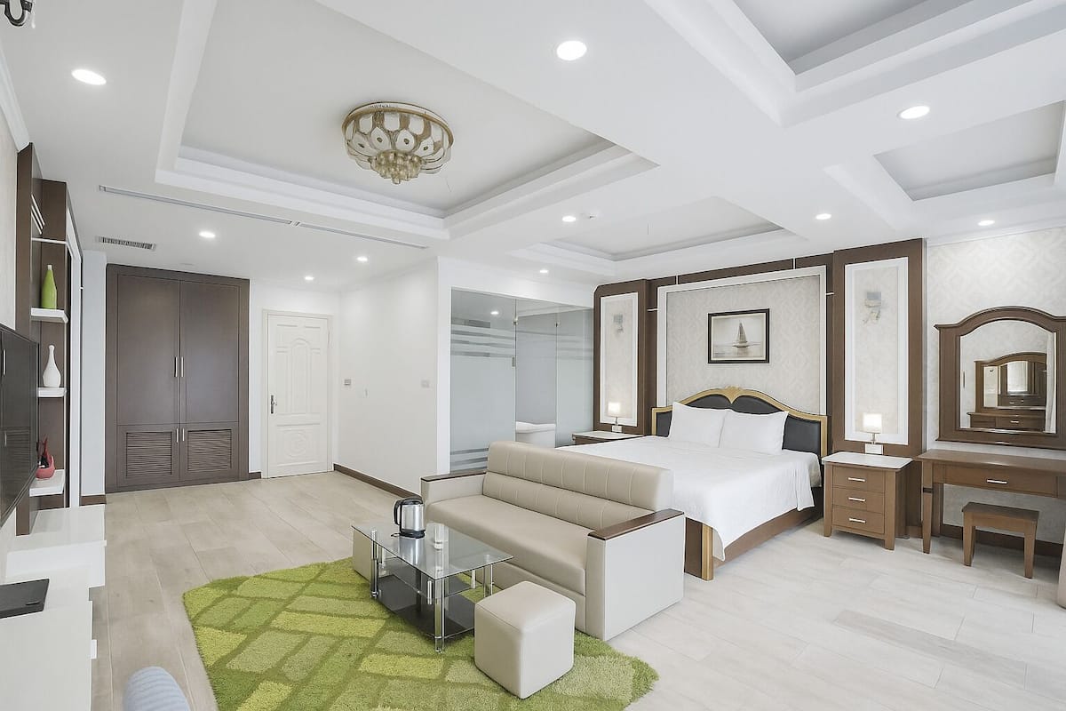 A modern hotel room with a bed, bedside table, dresser, and a seating area with a coffee table.