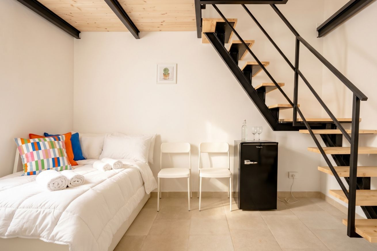 Une chambre à coucher avec un lit, des chaises blanches, un réfrigérateur noir et un escalier en bois.