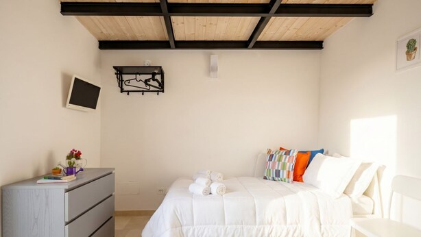 A bedroom with a bed, a dresser, a chair, a TV, and a wall-mounted shelf. - Casa di Lu - Modern Soul (Bari)