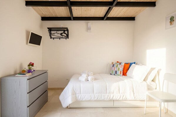 Une chambre à coucher comprenant un lit, une commode, une chaise, un téléviseur et une étagère fixée au mur.