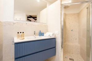 A bathroom with a shower, a sink with toiletries, and a mirror.