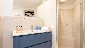 Un baño con ducha, lavamanos y artículos de aseo, y un espejo.