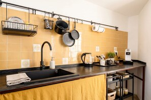 Une cuisine avec un plan de travail noir, un évier, une machine à café et des casseroles suspendues.