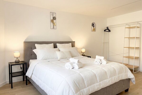 A neatly made bed with white bedding, two bedside tables with lamps, and a white wardrobe with shelves.