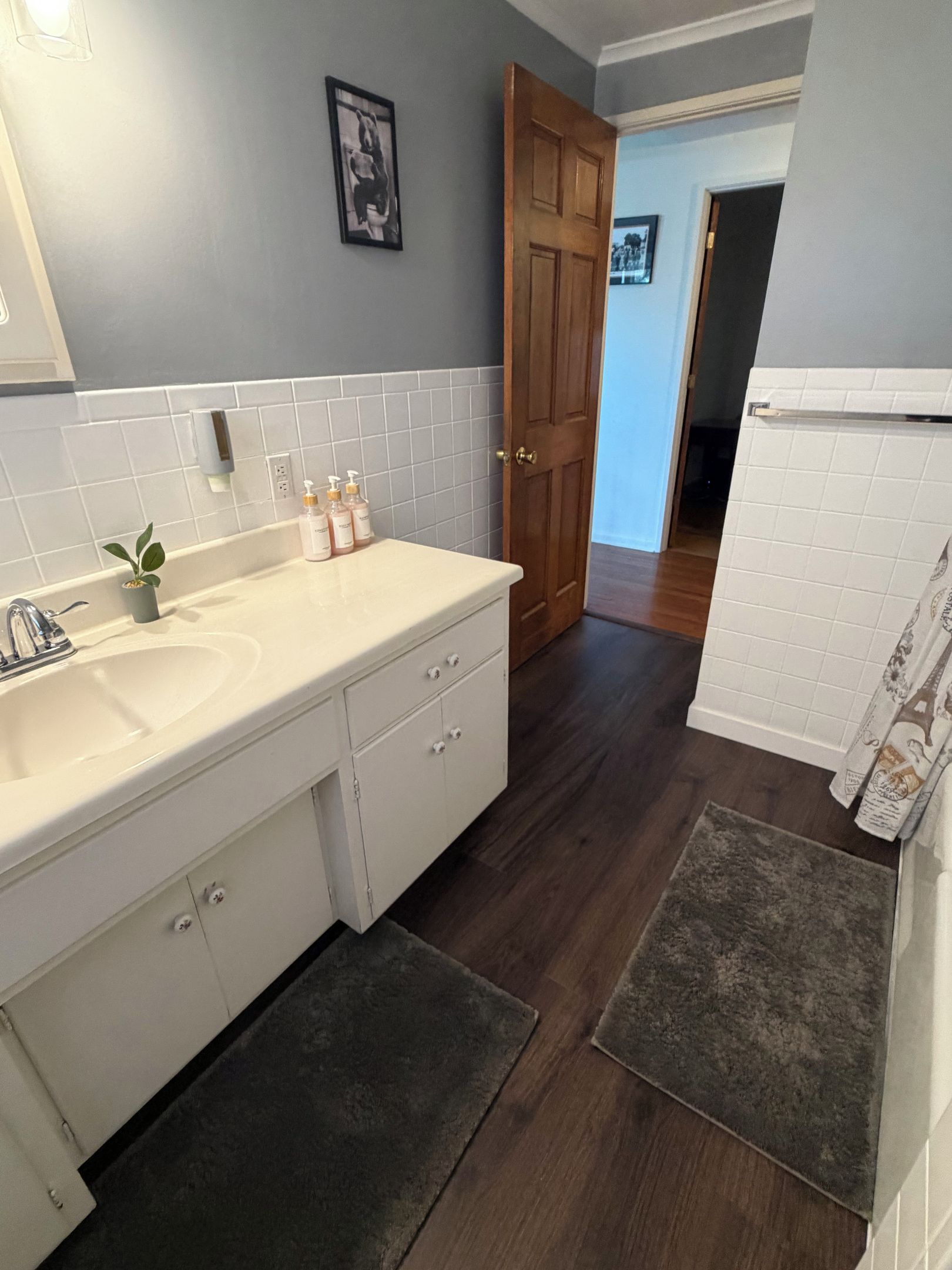 A bathroom with a white sink, wooden cabinet, and a door leading to another room.
