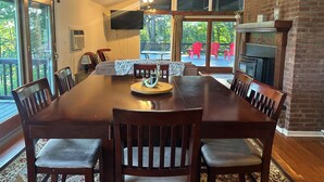 A dining room with a large wooden table, six chairs, a television, and a fireplace. - Bearberry Suite @Cooperstown Lodge-3mi to CDP+Pool (Cooperstown)