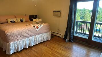 Une chambre dotée d’un grand lit, d’un ventilateur de plafond, d’une fenêtre avec des rideaux et offrant une vue sur la verdure environnante.