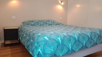 Una cama con una colcha estampada, dos lámparas de pared, una mesita de noche y un enchufe.