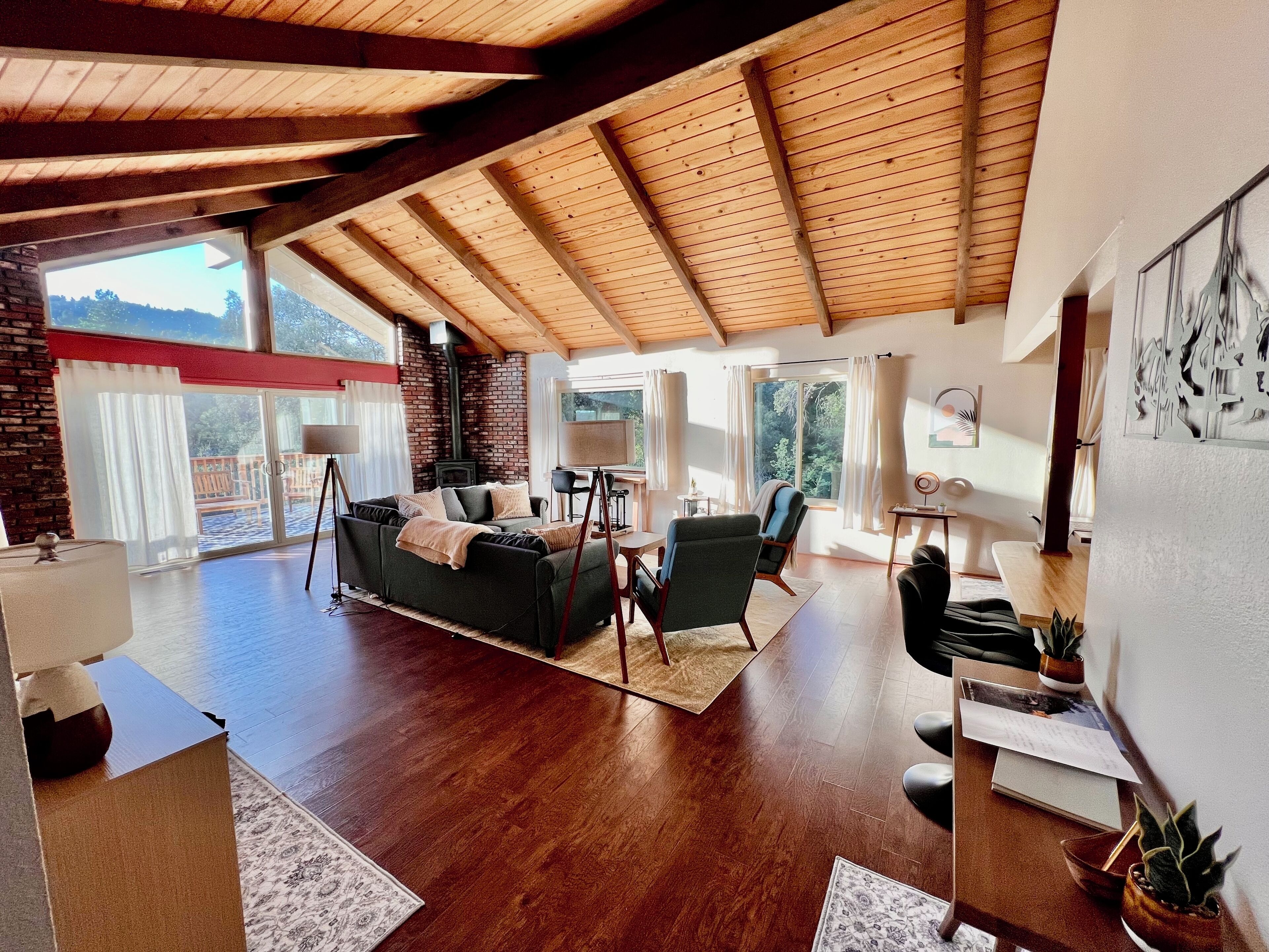 Un'ampia zona giorno con soffitto in legno, un camino e una grande finestra con vista su una terrazza.