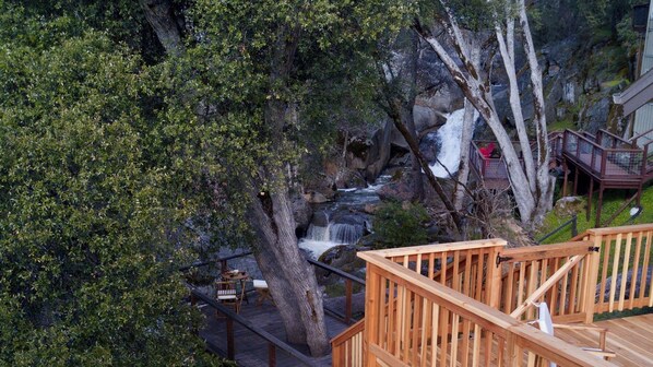 Eine Holzterrasse mit Blick auf einen Wasserfall und dichtes Grün.