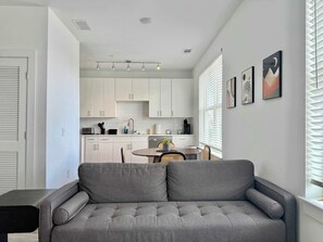 A modern living room with a grey sofa, a dining area with a round table, and a kitchen with white cabinets. - Renovated Penthouse in Old Fourth Ward (Atlanta)