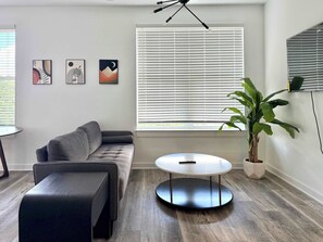 A modern living room with a grey sofa, a round coffee table, and a potted plant. - Renovated Penthouse in Old Fourth Ward (Atlanta)