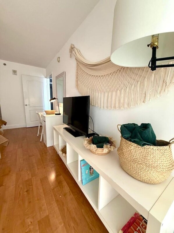 Una sala de estar moderna con un televisor de pantalla plana, una consola blanca, un tapiz de macramé y una cesta tejida.