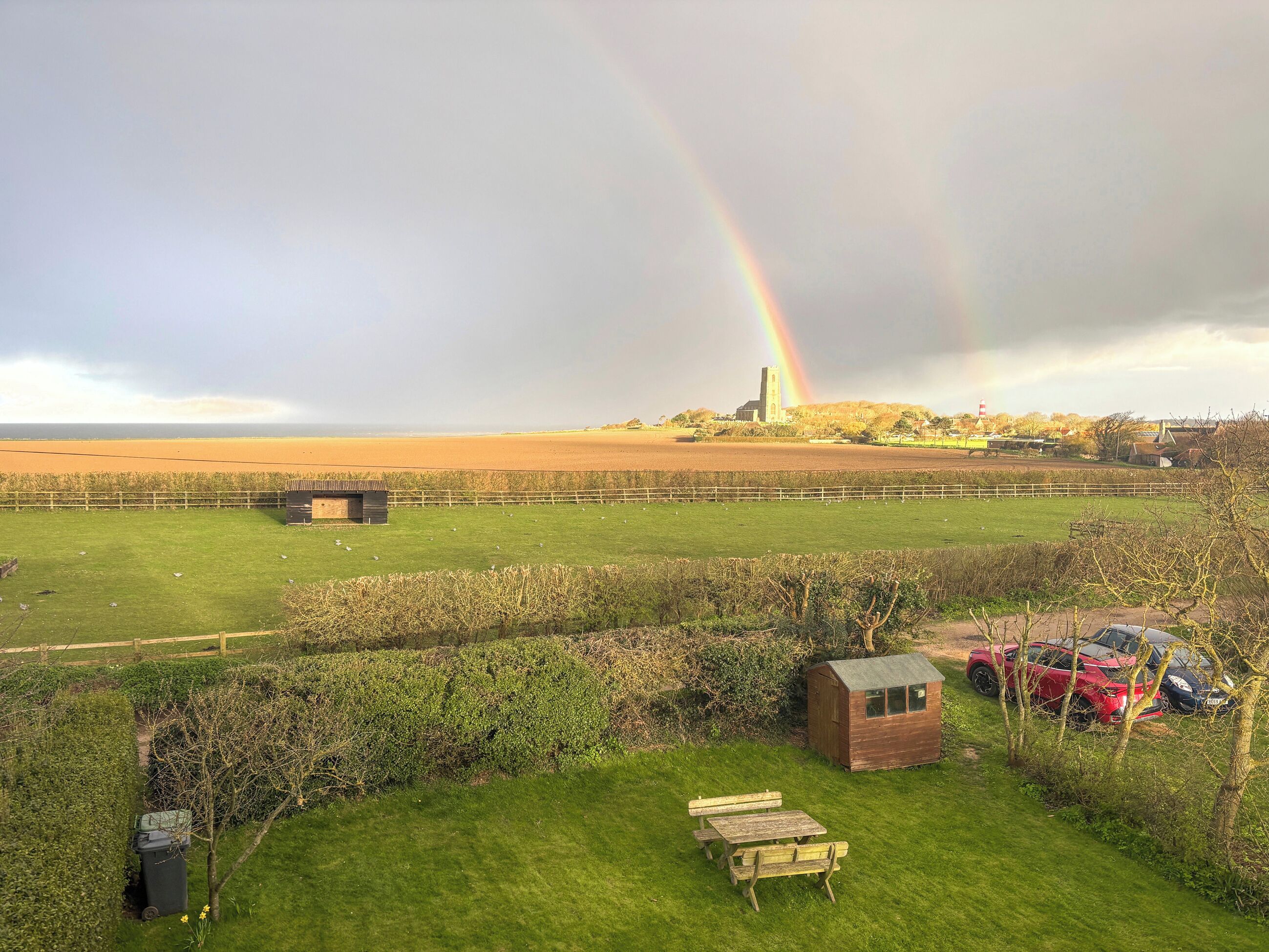 Ein grünes Feld mit einem Picknicktisch, einer kleinen Scheune und einem in der Ferne liegenden Gebäude mit einem Turm.