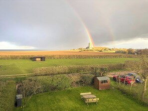 A grassy field with a picnic table, a small shed, and a distant building with a tower. - 3 bedroom accommodation in Happisburgh (Happisburgh)