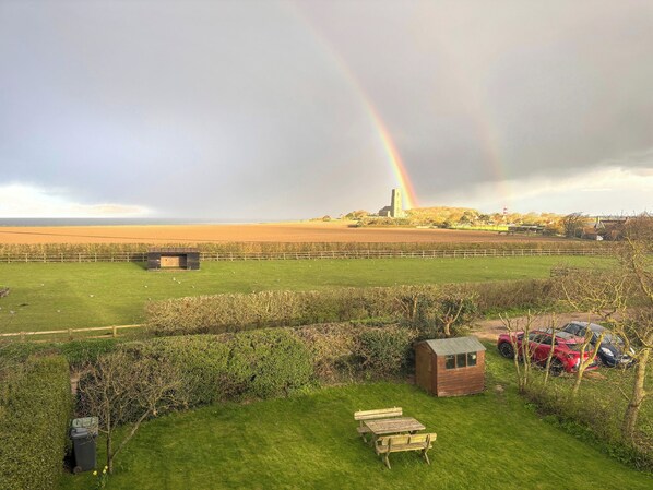 A grassy field with a picnic table, a small shed, and a distant building with a tower. - 3 bedroom accommodation in Happisburgh (Happisburgh)