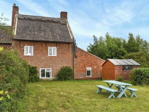 Une maison en briques avec un toit de chaume, une extension en bois et une table de pique-nique dans la cour.