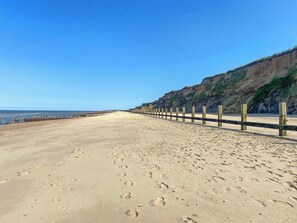 Une plage de sable bordée de poteaux en bois, un ciel dégagé et une falaise en arrière-plan.