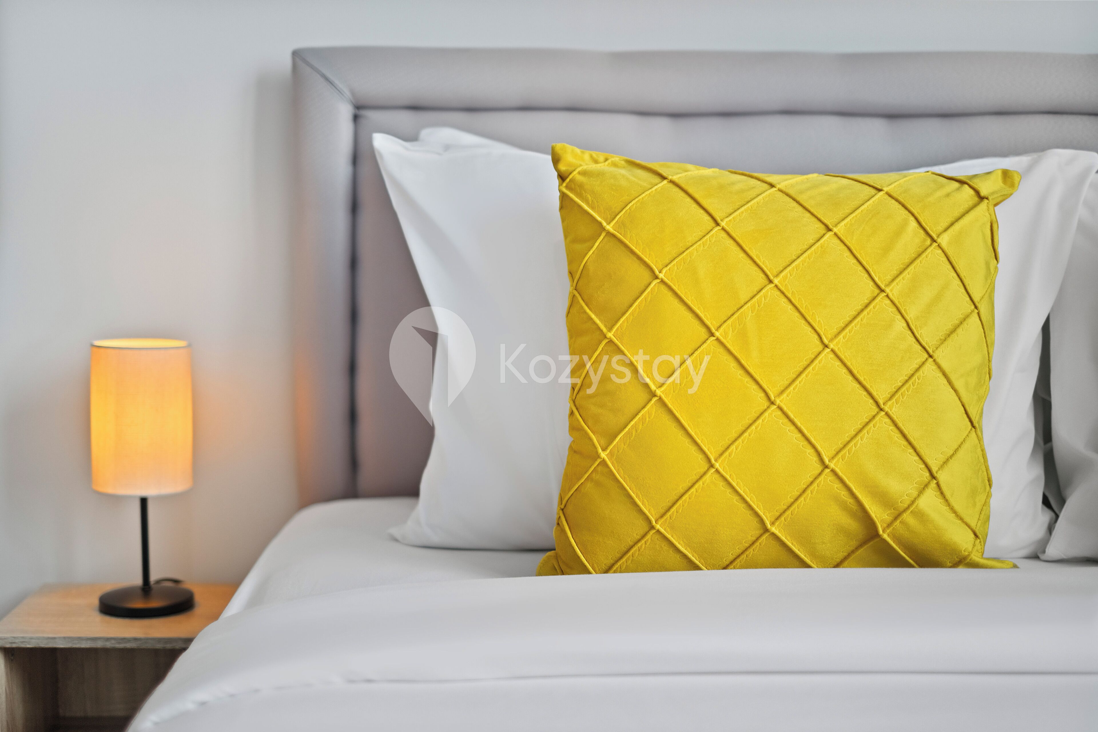 A bed with white and yellow pillows, a bedside lamp, and a grey headboard.