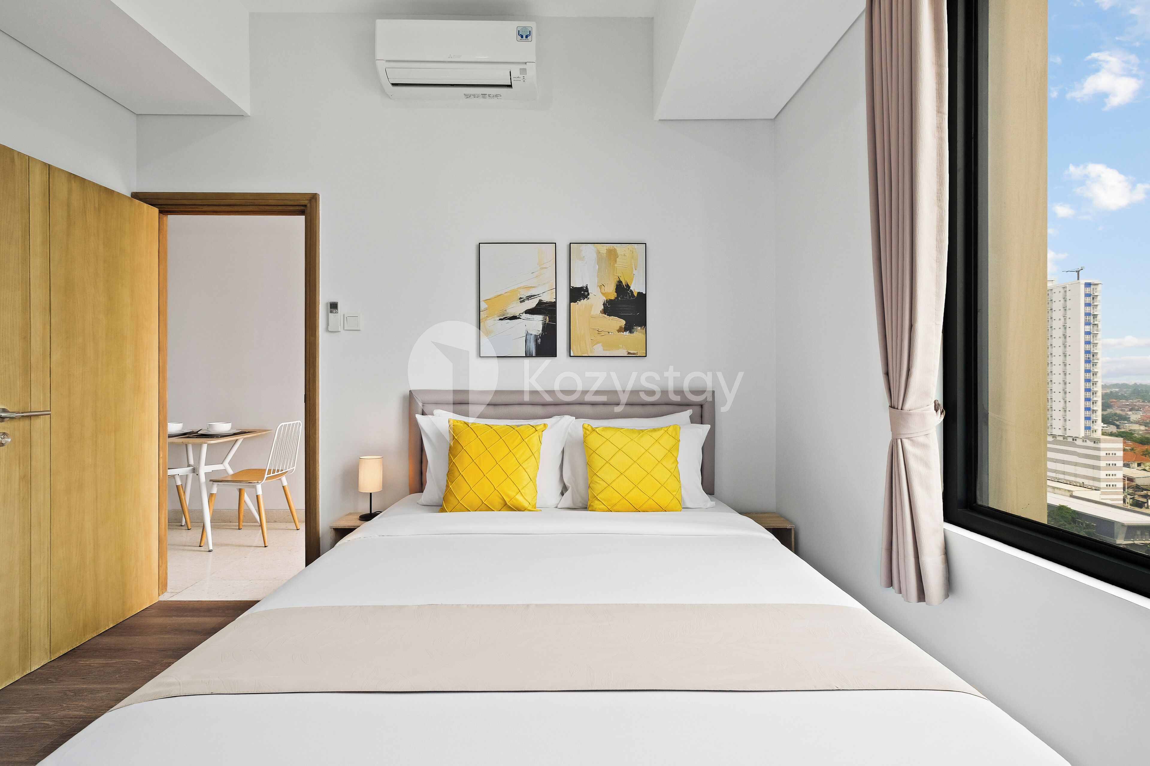 Una habitación de hotel moderna con una cama, una ventana con cortinas, un escritorio con una silla y vistas a edificios.