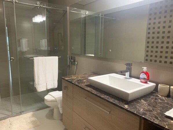 A modern bathroom with a glass-enclosed shower, a white sink, and a large mirror.