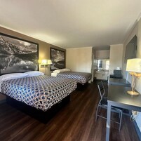 Habitación de hotel con dos camas, un escritorio, una silla y un espejo grande.