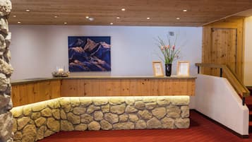 Un área de recepción con pared de piedra, paneles de madera, un cuadro enmarcado y un jarrón con flores.