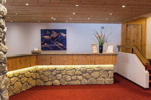 A reception area with a stone wall, wooden paneling, a framed painting, and a vase with flowers. - TOP Hotel San Gian St. Moritz (St. Moritz)