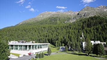 A modern building with a glass facade, surrounded by a well-maintained lawn and a forested mountain backdrop.