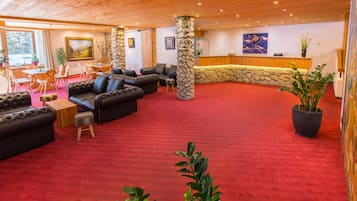 Un vestíbulo amplio con alfombra roja, sofás de cuero, un pilar de piedra y una mesa de recepción.