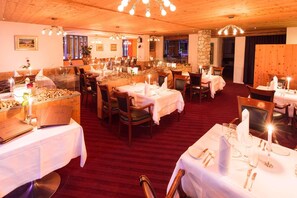 A restaurant with multiple tables set for dining, wooden ceiling, and a stone wall. - TOP Hotel San Gian St. Moritz (St. Moritz)