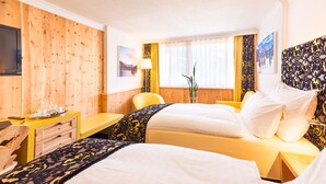 A hotel room with two beds, a wooden wall, a TV, a desk, and a window with curtains. - TOP Hotel San Gian St. Moritz (St. Moritz)
