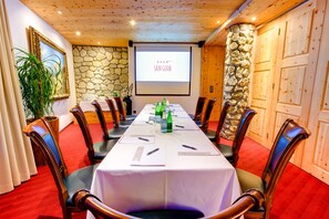 A conference room with a long table, chairs, a projector screen, and a stone wall. - TOP Hotel San Gian St. Moritz (St. Moritz)