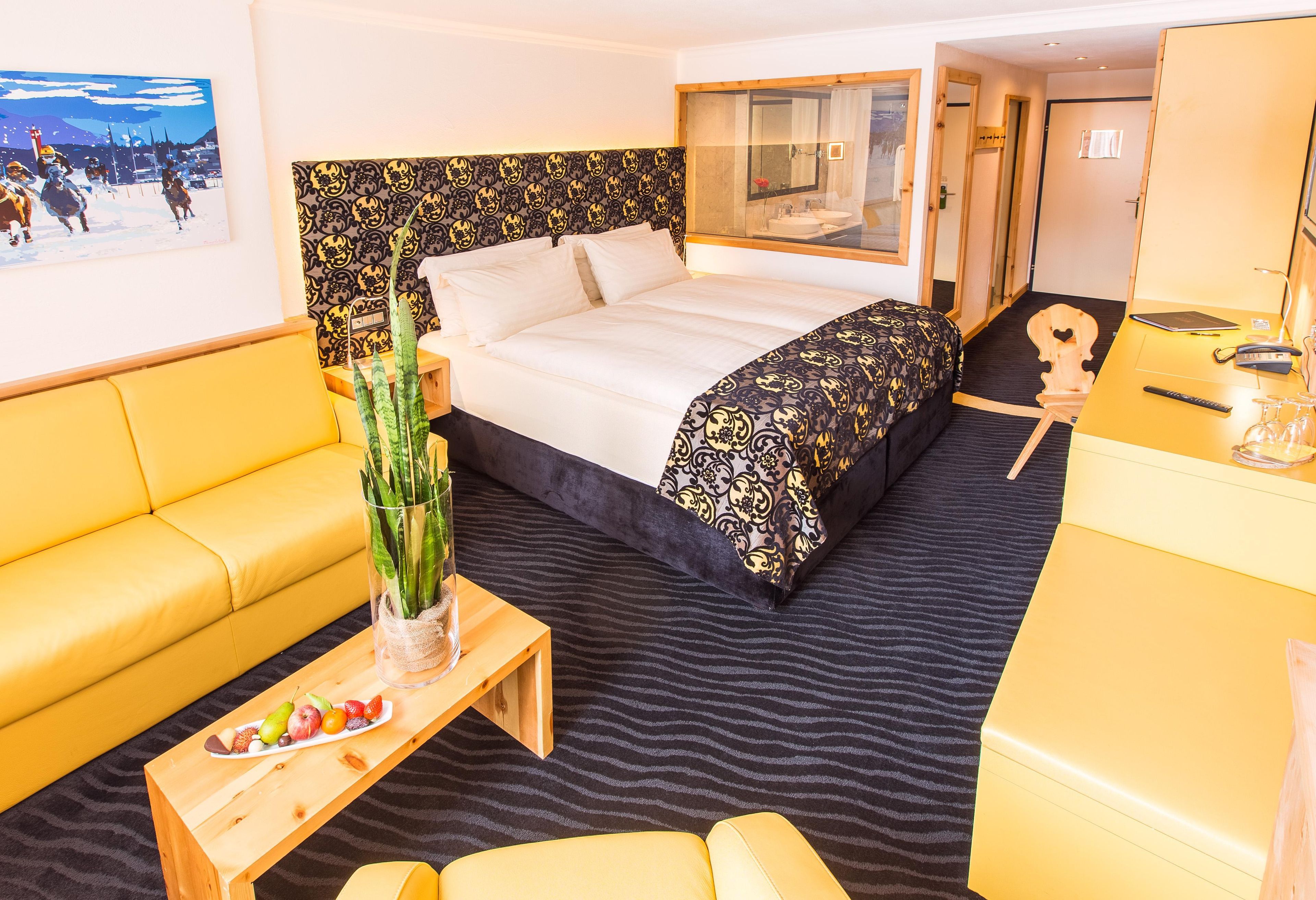 Ein Hotelzimmer mit Bett, einer Sitzecke, einem kleinen Tisch mit Obst, einer Pflanze und einem Spiegel.