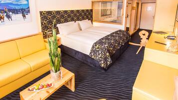 Ein Hotelzimmer mit Bett, einer Sitzecke, einem kleinen Tisch mit Obst, einer Pflanze und einem Spiegel.