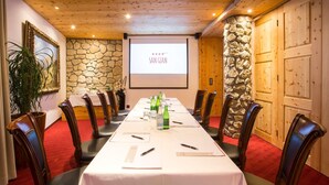 A conference room with a long table, chairs, a projector screen, and a stone wall. - TOP Hotel San Gian St. Moritz (St. Moritz)