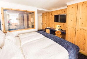 A hotel room with a large bed, a wooden wardrobe, a television mounted on the wall, and a small desk with a telephone. - TOP Hotel San Gian St. Moritz (St. Moritz)