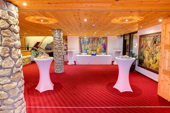 Une pièce avec une moquette rouge, des tables blanches, un pilier en pierre et un escalier en arrière-plan.