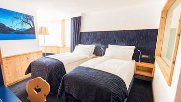 Habitación de hotel con dos camas, un escritorio, una silla, una lámpara y un ventanal con vistas a una montaña y un lago.