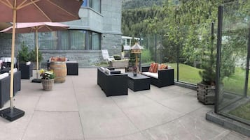 Un patio al aire libre con mobiliario moderno, un paraguas grande y vistas a un paisaje montañoso.