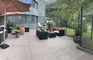 An outdoor patio area with modern furniture, a large umbrella, and a view of a mountainous landscape. - TOP Hotel San Gian St. Moritz (St. Moritz)