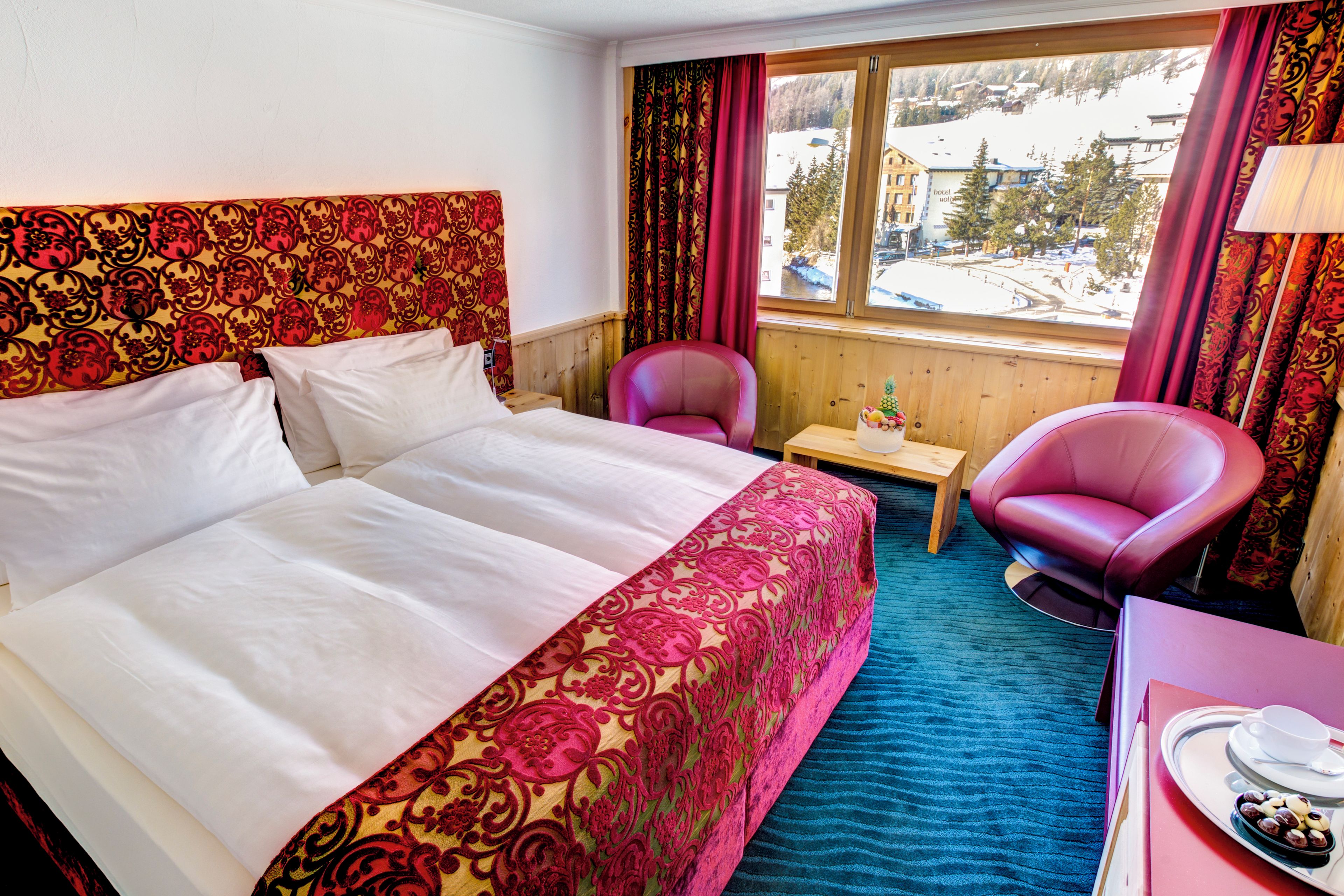 A hotel room with a large bed, a small table, two chairs, and a view of a snowy landscape.