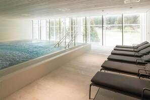 An indoor swimming pool with clear glass walls, a tiled floor, and sun loungers. - TOP Hotel San Gian St. Moritz (St. Moritz)