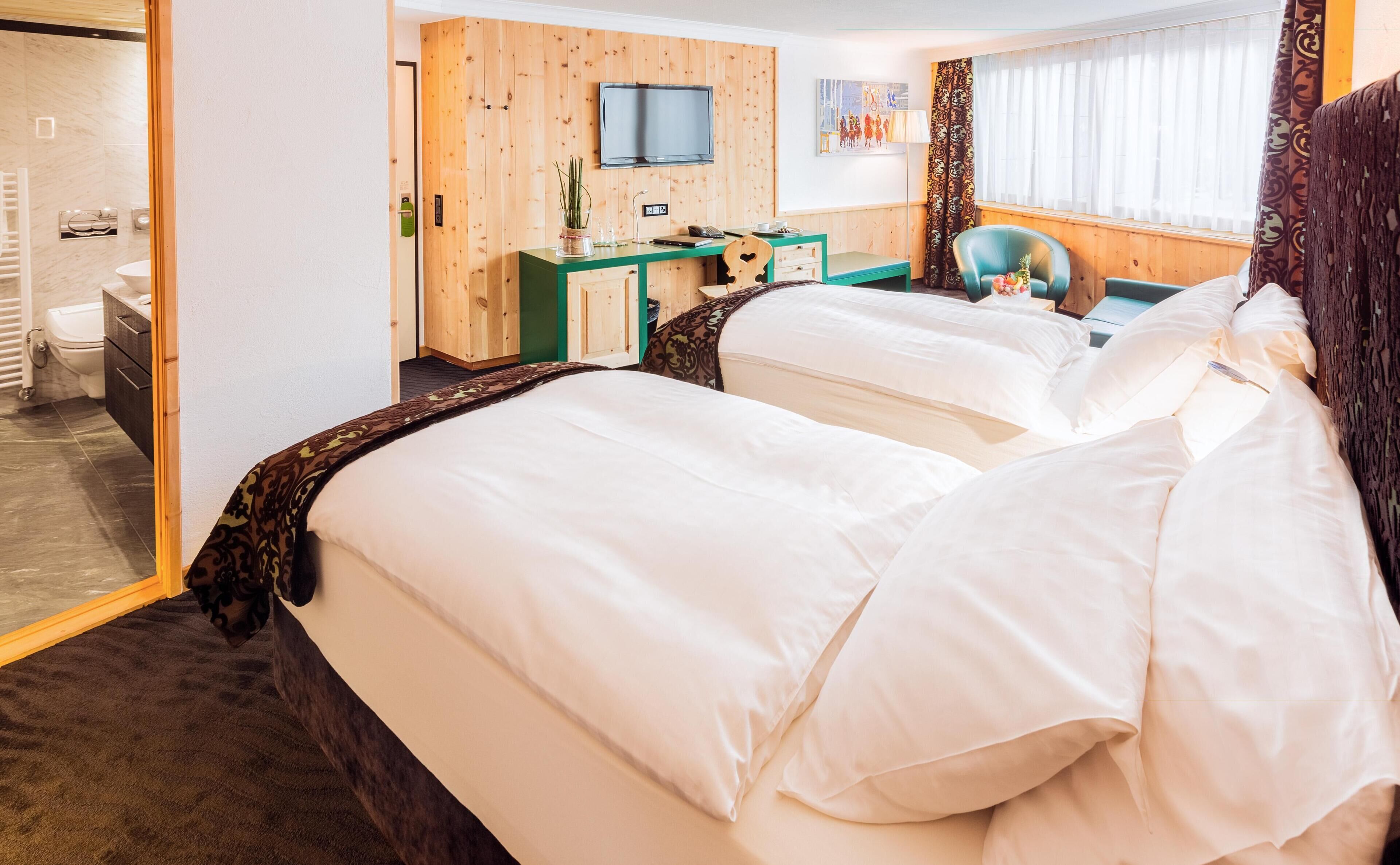 A hotel room with two beds, a desk, a chair, a television, and a window with curtains.