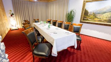A conference room with a long table, chairs, a red carpet, a painting, and a plant.