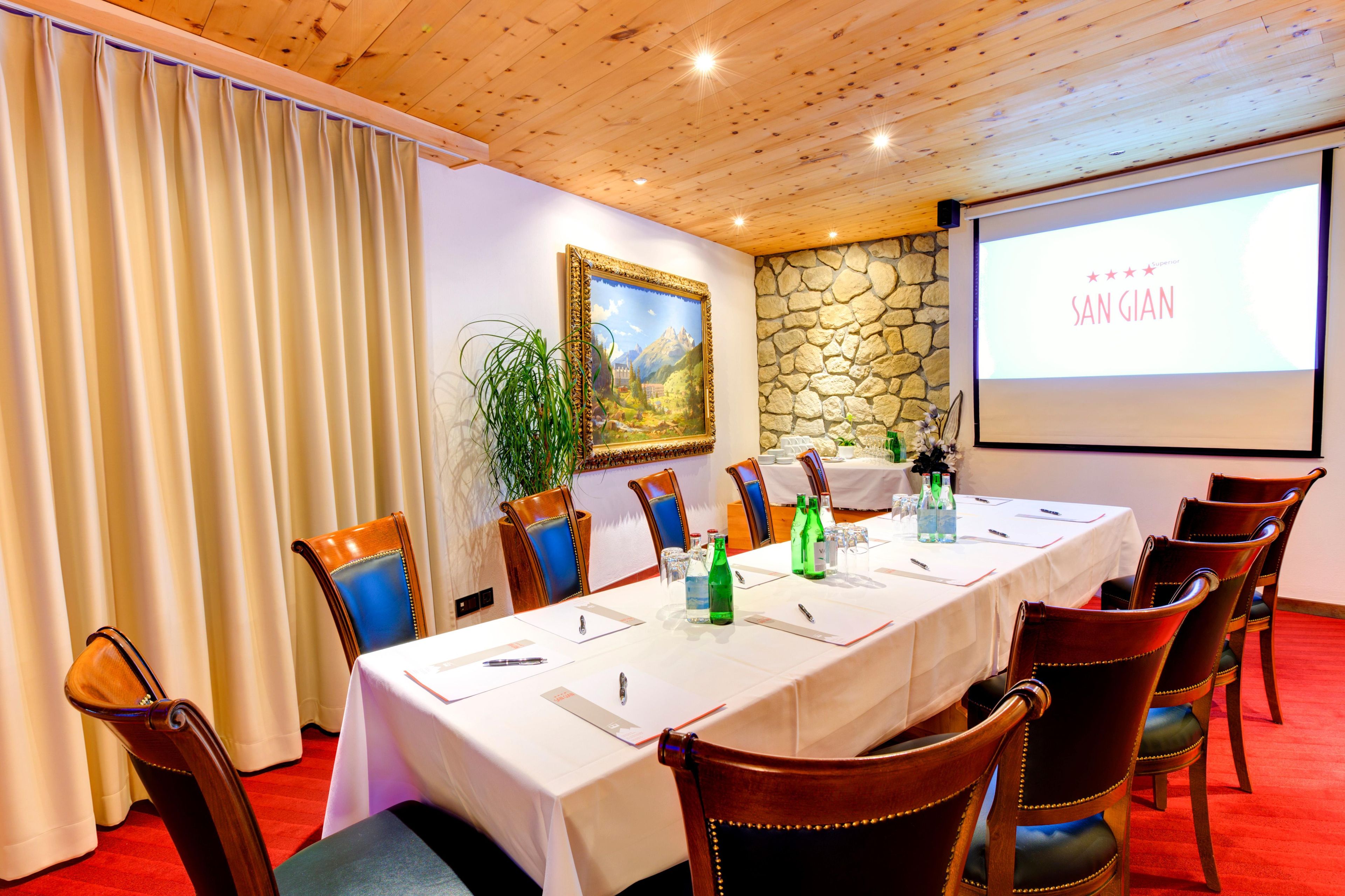 A conference room with a long table, chairs, a projector screen, and a stone wall.