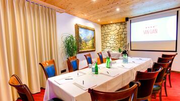 A conference room with a long table, chairs, a projector screen, and a stone wall.