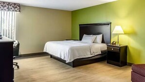 Une chambre d’hôtel comprenant un lit, une table de chevet, une lampe et un bureau avec une chaise.