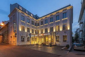 A corner building with a sign reading "HOTEL" and "RESTAURANT." It has multiple windows and a well-lit entrance. - Ratonda Centrum Hotel (Vilnius)